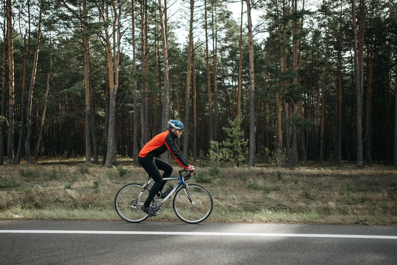 Road cyclist in full kit training on an open forest-lined road