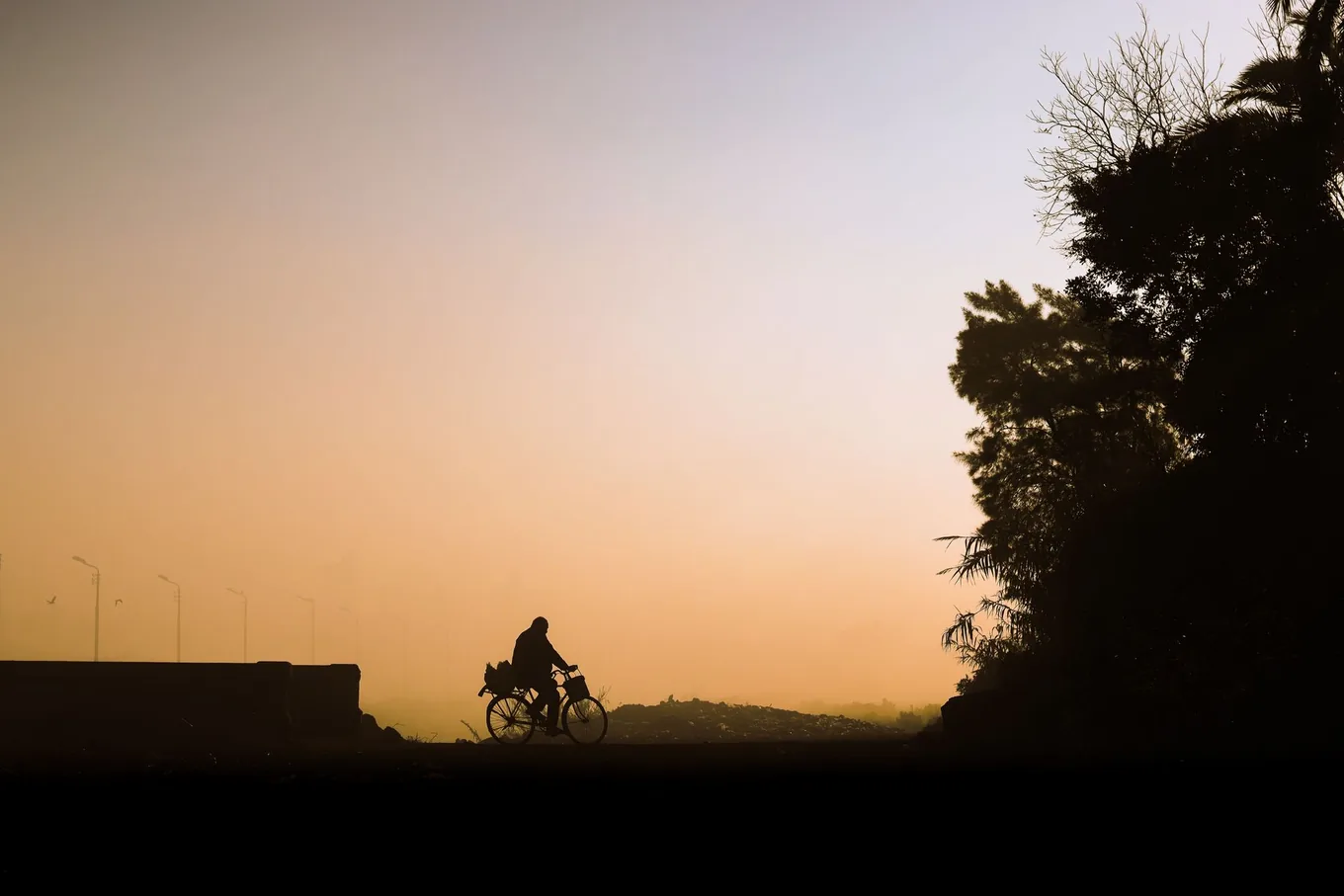 Cyclist riding at dawn through thick, smoke-hazed orange air