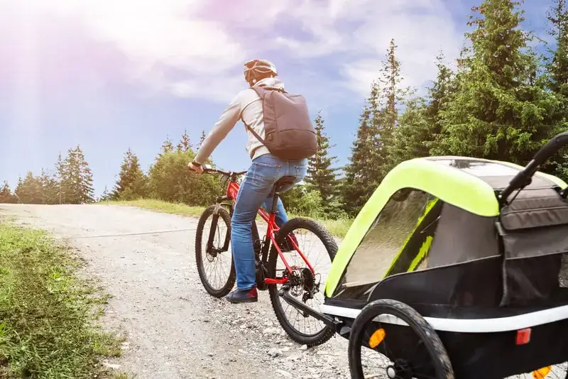 Bike towing a child trailer Cyclist in a helmet towing a covered two-wheel child trailer up a gravel path, the tow bar attached at the rear axle