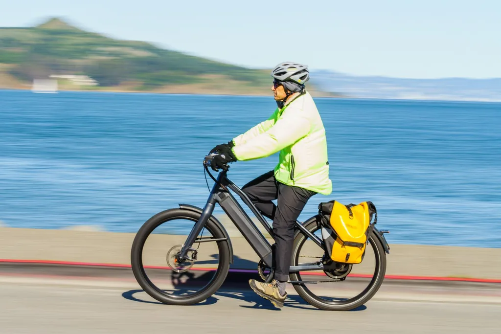 Helmeted commuter on an e-bike along the shoreline Commuter wearing a helmet riding an electric bike with a pannier along a shoreline road