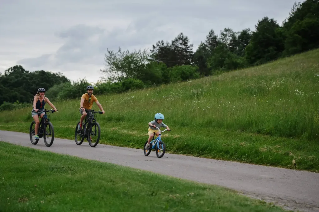 Helmeted family riding a paved path Family riding along a paved path, parents on e-bikes and a child on a small bike, all wearing helmets