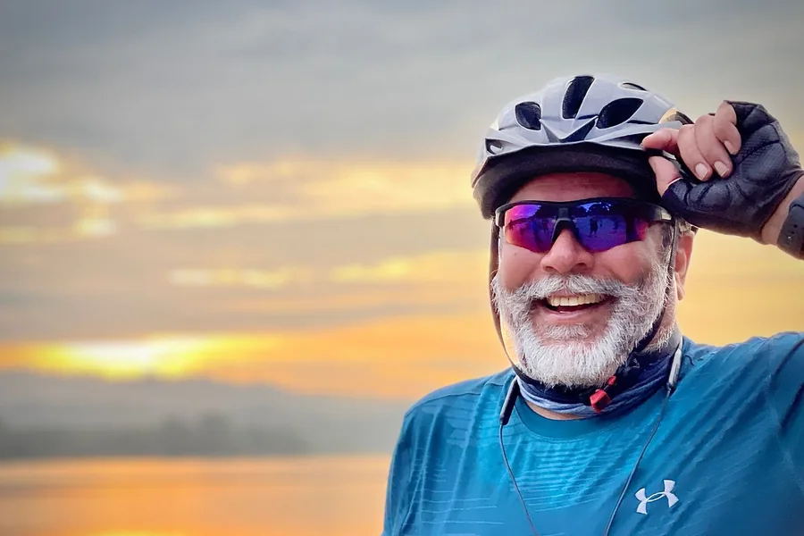 Smiling senior cyclist in a helmet at a lakeside sunset