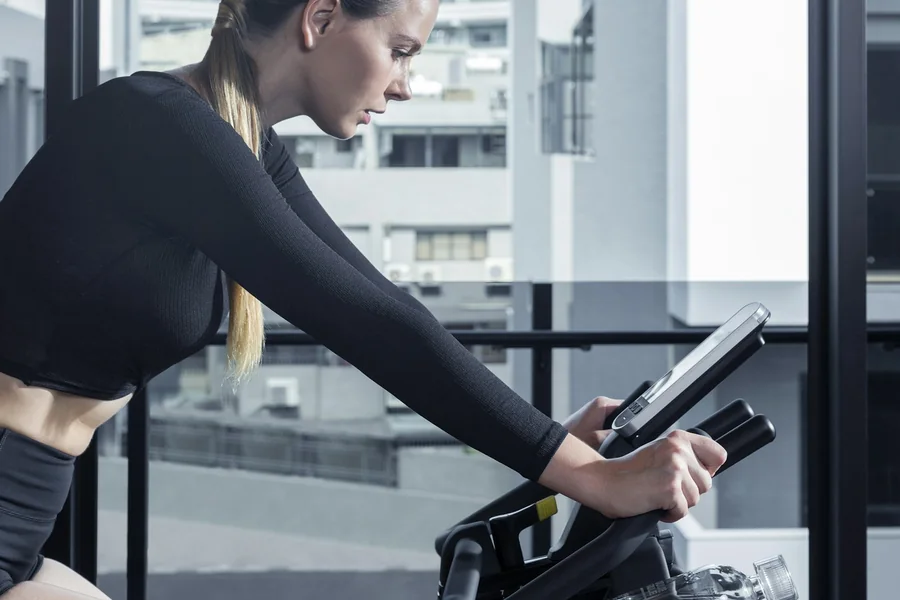 Cyclist riding indoors, leaning forward to adjust a workout on the screen mounted at handlebar height