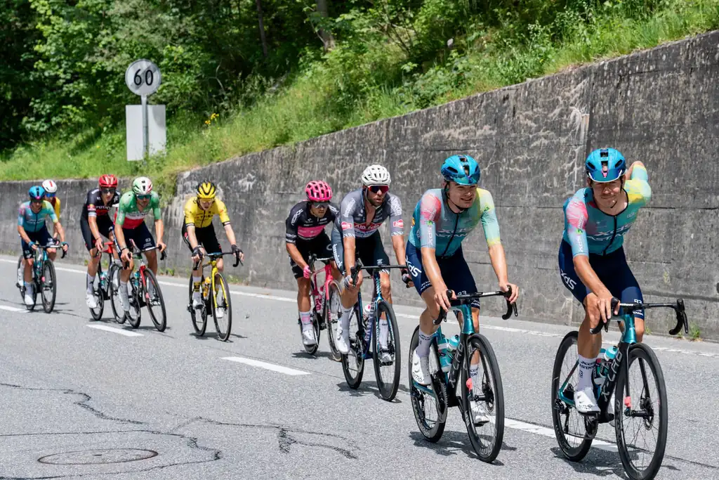 The surge: the pace jumps every time the road tilts up Professional cyclists racing uphill on a mountain road, the lead riders surging ahead of the group