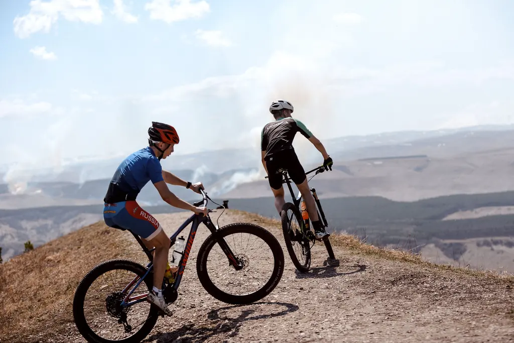 A fire road or doubletrack climb with a steady grade is best Two mountain bikers riding up a dirt doubletrack climb above a wide valley