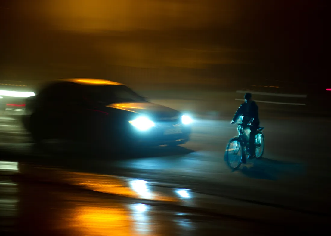 Standalone bicycle insurance covers crash damage, theft, and liability that auto policies leave out Cyclist riding on a wet city street at night as a car approaches with its headlights on
