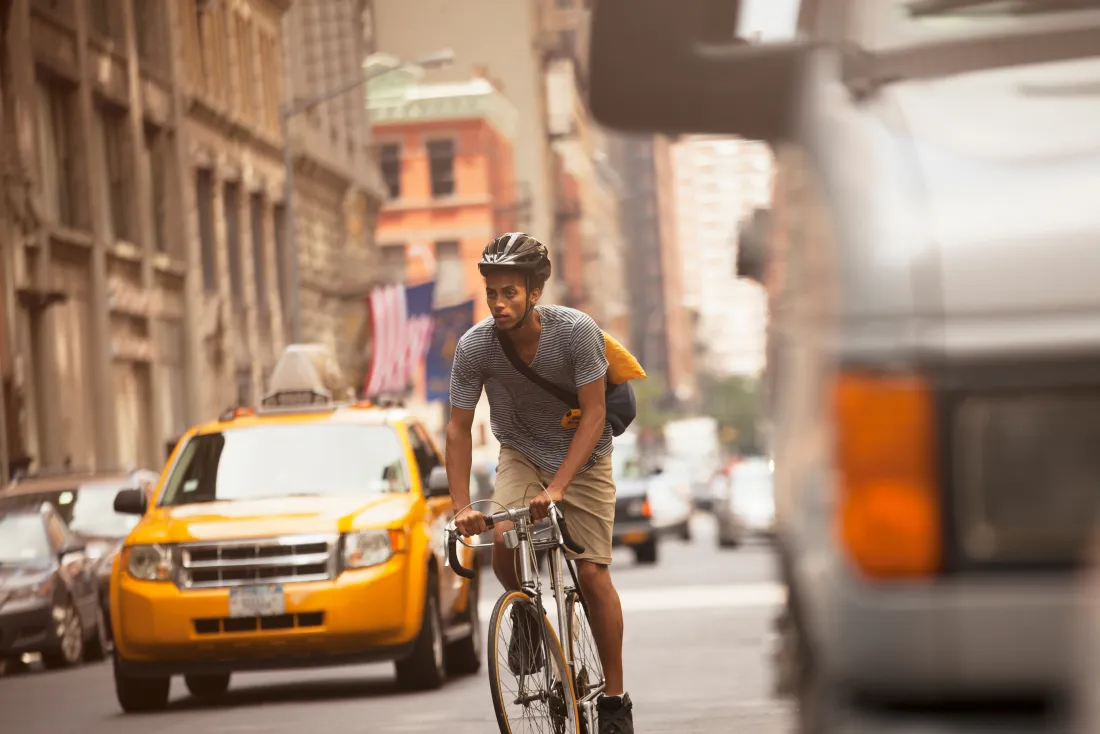 In no-fault states a cyclist struck by a car is generally treated like a pedestrian and can claim PIP benefits Cyclist in a helmet riding through New York City traffic between a yellow taxi and a bus
