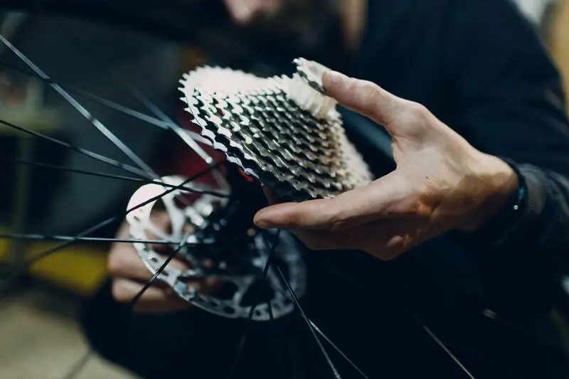 A mechanic holding a wide-range rear cassette mounted on a bicycle wheel, showing the difference in size between the smallest and largest cogs
