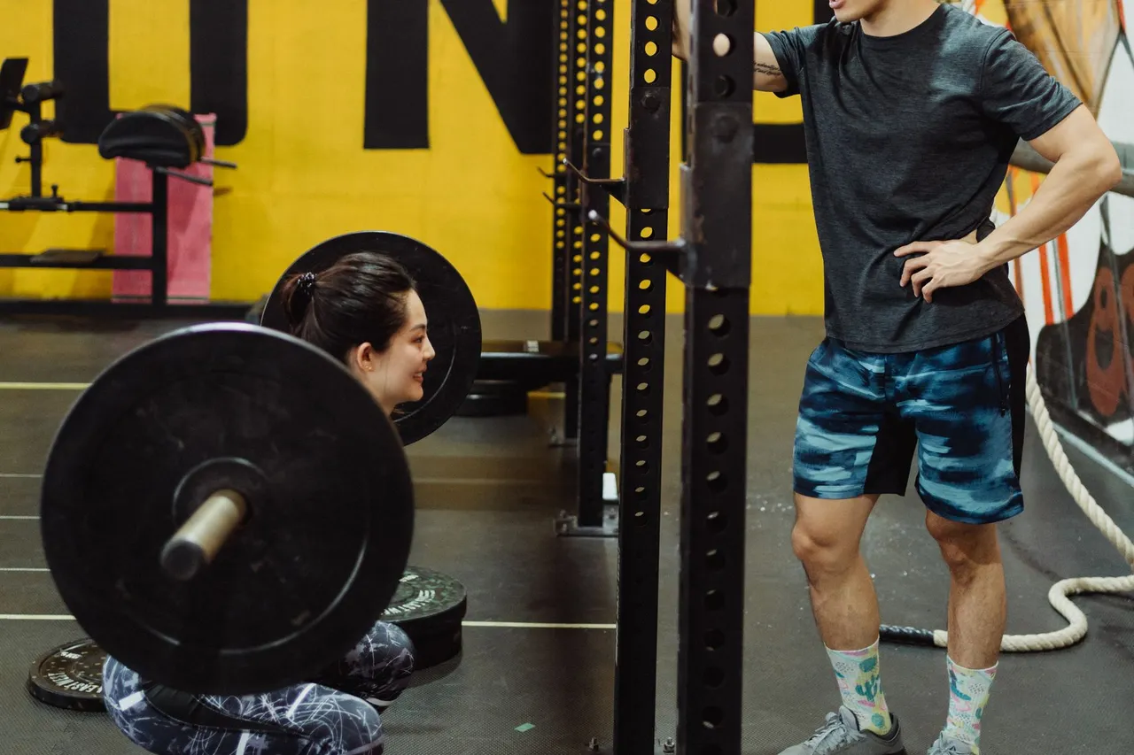 Heavy strength work makes every watt cheaper Athlete at the bottom of a heavy barbell back squat in a gym while a coach looks on