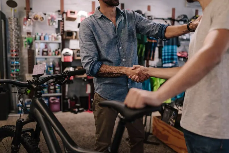 Buyer and seller shaking hands over a bicycle in a bike shop