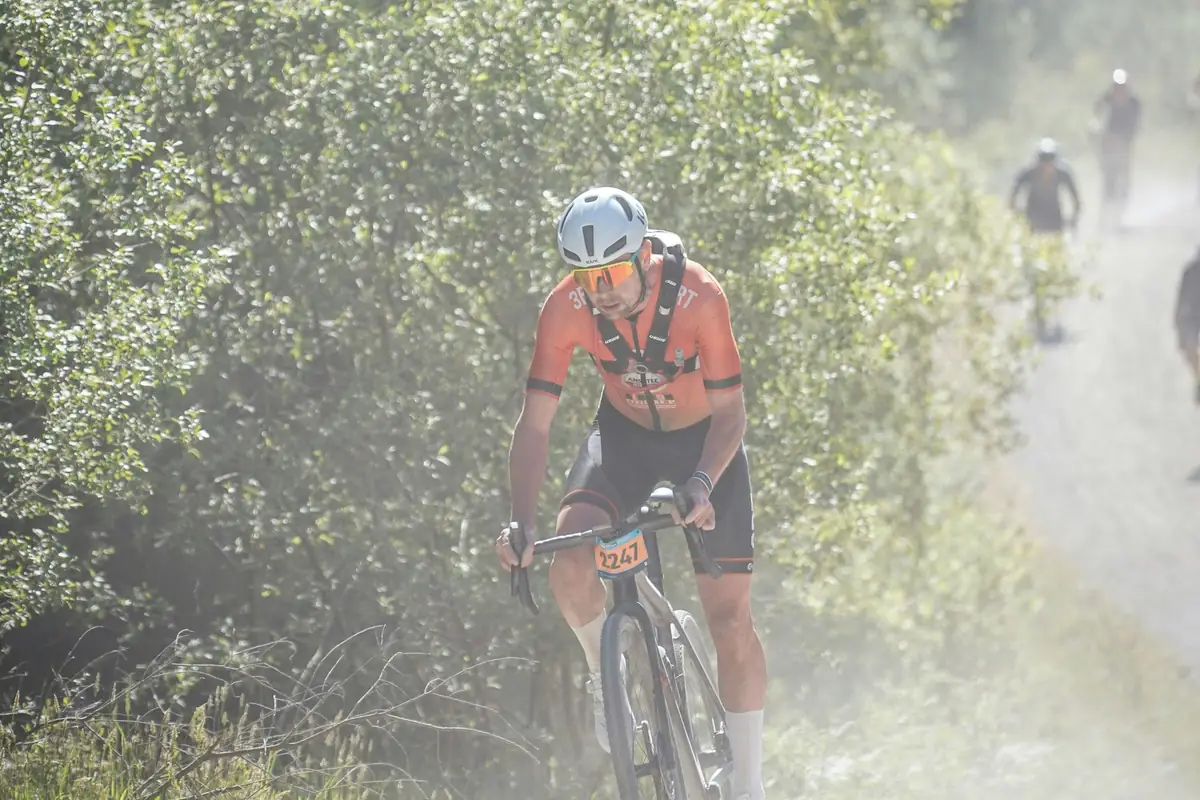 Cyclist in a race number grinding up a dusty gravel climb, a hard interval effort