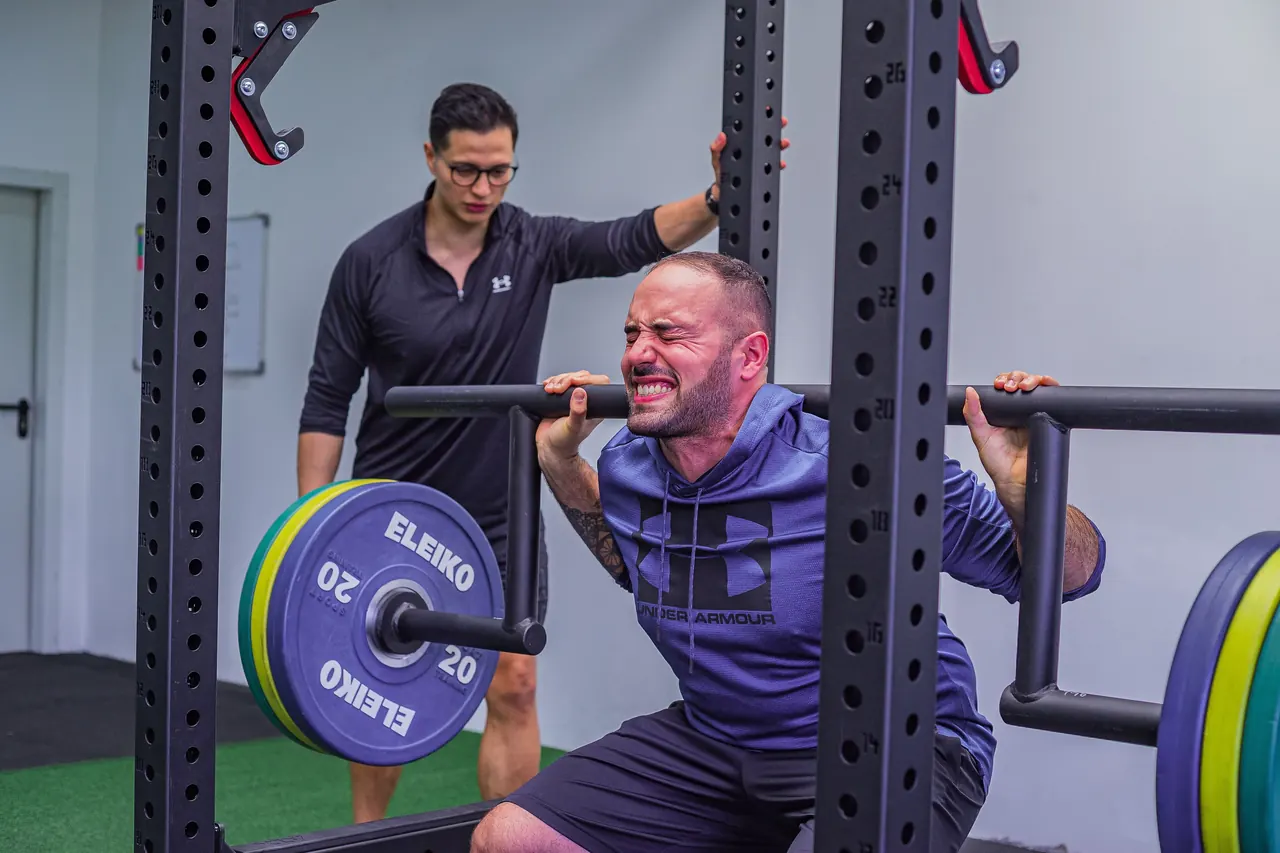 Heavy slow resistance: three gym sessions a week for twelve weeks Man squatting a heavy barbell in a power rack while a coach watches his form