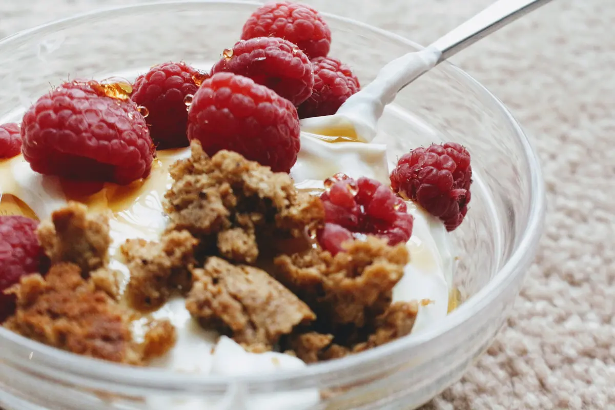 Bowl of Greek yogurt with raspberries and granola, a slow-digesting protein serving before bed