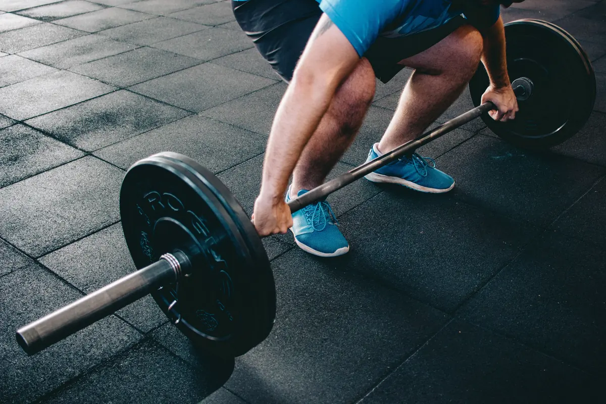 Close-up of a lifter gripping a loaded barbell on a rubber gym floor just before the pull Close-up of a lifter gripping a loaded barbell on a rubber gym floor just before the pull