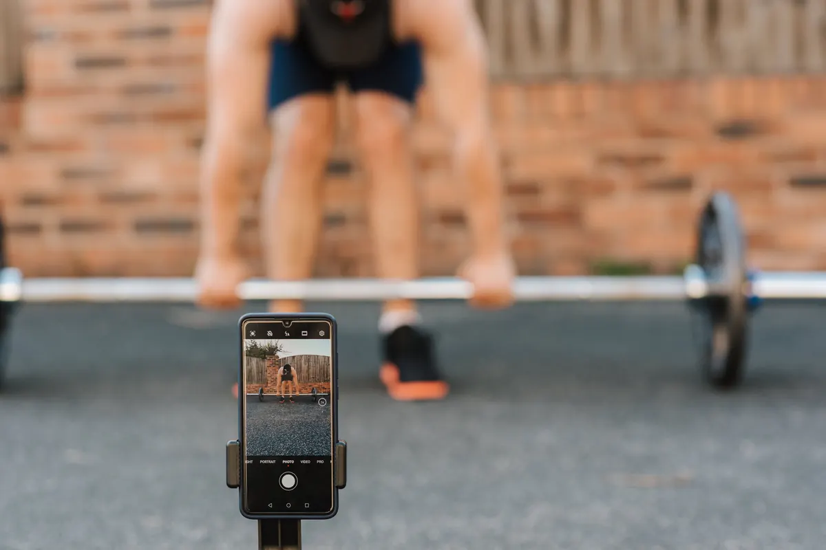 Smartphone on a small tripod filming a lifter deadlifting a barbell from the side at bar height Smartphone on a small tripod filming a lifter deadlifting a barbell from the side at bar height