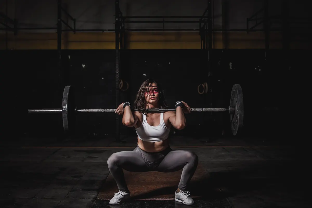 Woman at the bottom of a barbell back squat in a dimly lit gym, the kind of grinding rep velocity-based training cuts out Woman at the bottom of a barbell back squat in a dimly lit gym, the kind of grinding rep velocity-based training cuts out