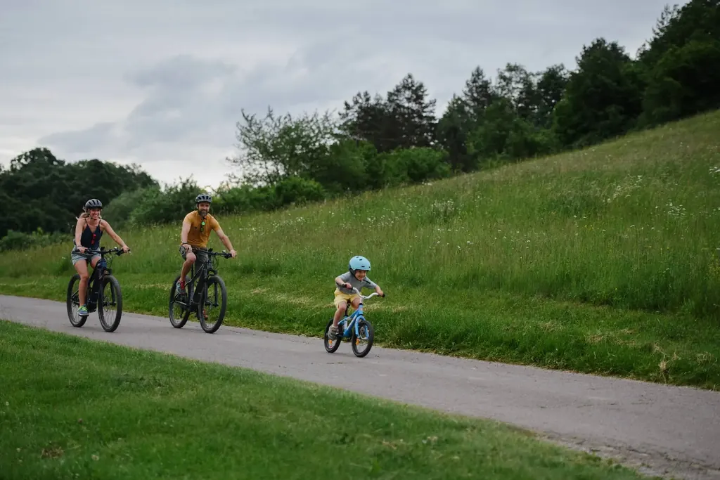 Family in helmets riding along a paved multi-use path, parents on e-bikes and a child on a small bike