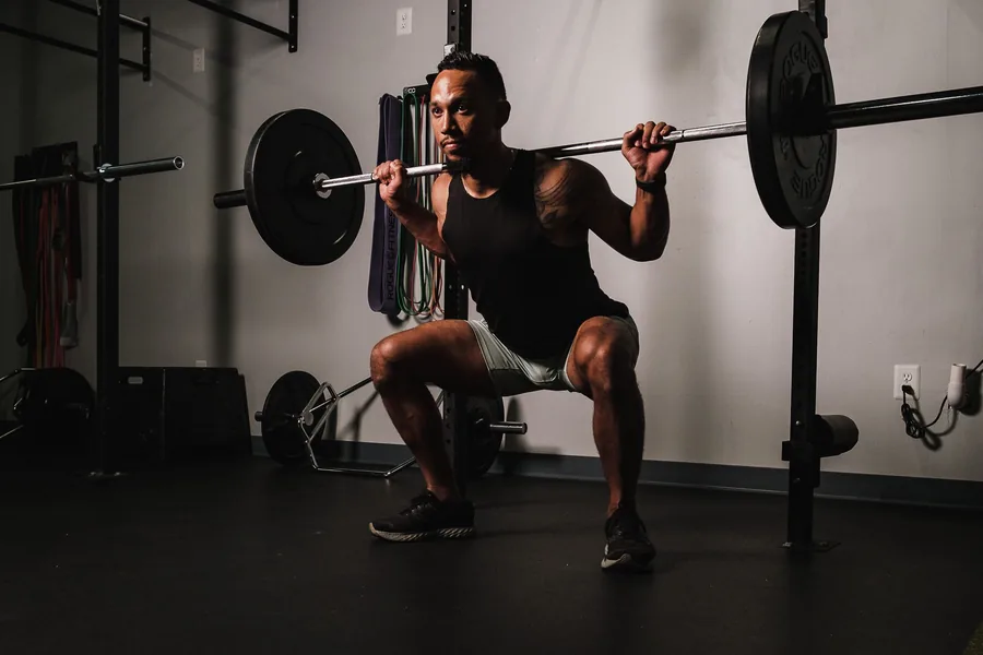The squat: the foundational movement for cycling strength Male athlete performing a barbell back squat in a home gym