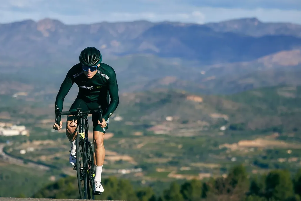 The full climb: one benchmark ascent every 10 to 14 days at the hardest even pace you can hold Road cyclist out of the saddle climbing a mountain road, the valley floor far below