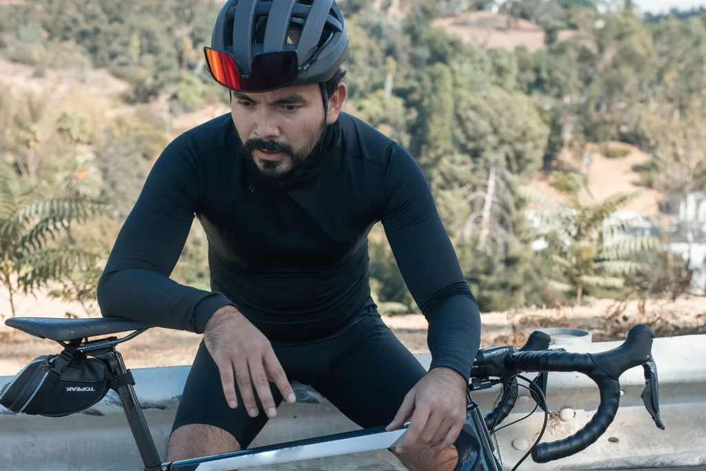 The fade after 90 minutes: the fix is the long steady ride you keep skipping, not another interval session Road cyclist in black kit sitting on a guardrail beside his bike, head down and hands on his knees after a long ride